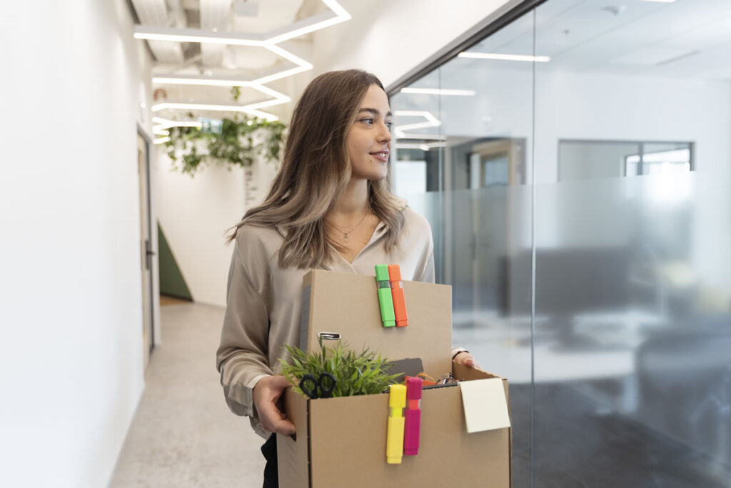 Young female solicitor leaving her office carrying a box of personal belongings after deciding to change legal jobs.