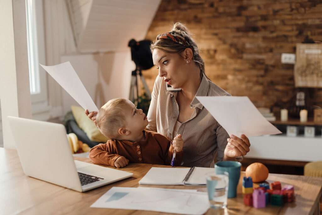 Young legal professional working from home in her kitchen while caring for her infant, highlighting work-life balance and flexible working in the legal profession.